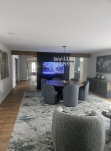 Modern dining area with a round table, gray chairs, large rug, and a built-in aquarium in the background.