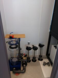 Aquarium filtration system with multiple filter units, PVC pipes, and a tape measure on a cardboard sheet.