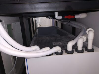 White pipes and hoses connect to a rectangular machine inside a building, with a control valve visible on top.
