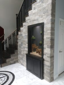 Built-in aquarium with rocks and plants set into a stone wall beside a staircase in a modern home interior.