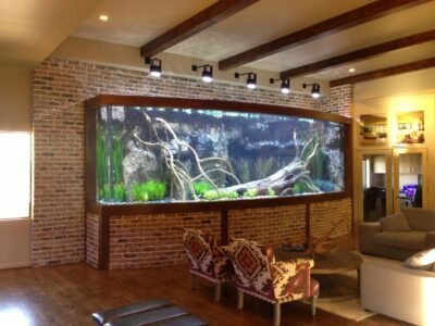 Large built-in aquarium with plants and driftwood set in a brick wall in a modern living room with wooden beams.