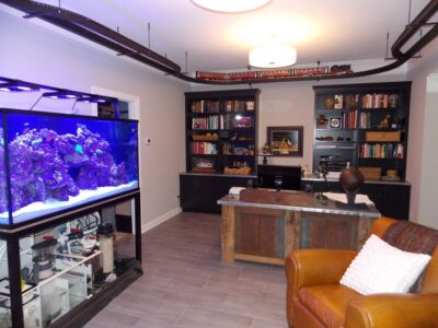 Home office with bookshelves, large aquarium on the left, wooden desk, and a model train on tracks near the ceiling.