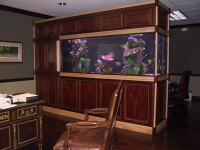 Large built-in aquarium in a wood-paneled office, with a wooden desk, chair, and books visible in the foreground.
